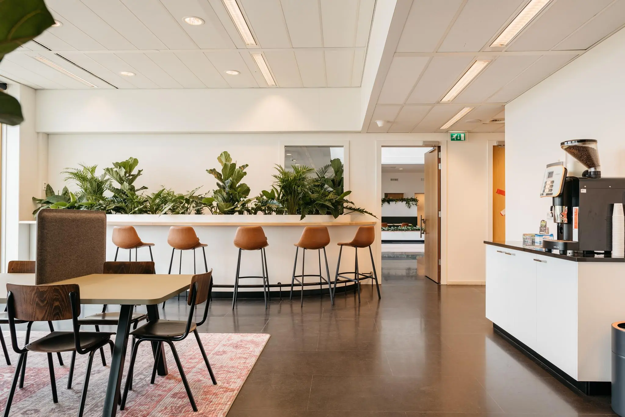 Moderne en lichte kantoorlounge aan de Fascinatio Boulevard met zithoeken, barkrukken, veel planten en een koffieautomaat.
